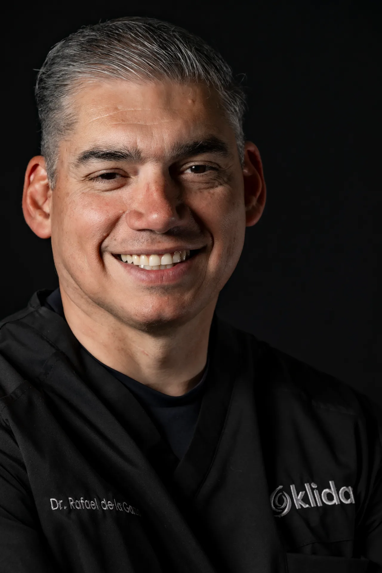 Dr. Francisco Rafael De La Garza González sonriendo, retrato de estudio sobre fondo oscuro